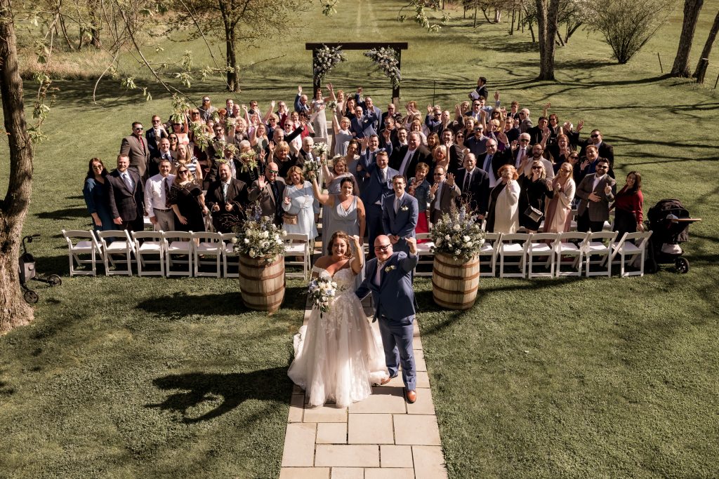 Bride and groom smiling at the end of the aisle with wedding guests cheering behind them taken by wedding photographer.