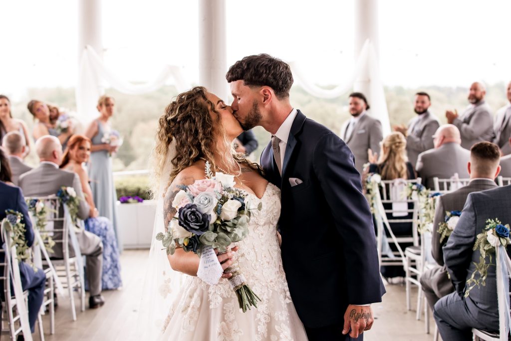 Bride and groom share a kiss at the altar surrounded by soft lighting and end of aisle by wedding photographer.