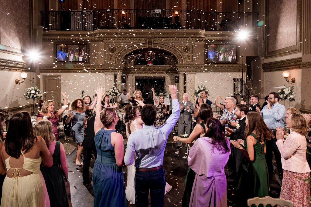 Wedding guests dancing under a shower of confetti on a packed dance floor during the reception celebration shot by wedding photographer.